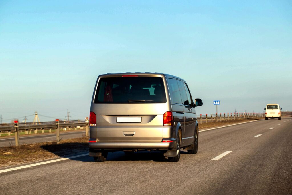 Rückansicht des silbernen Minivans, der auf einer asphaltierten Autobahn unter klarem blauen Himmel fährt, Leitplanke am Straßenrand, andere Fahrzeuge in der Ferne